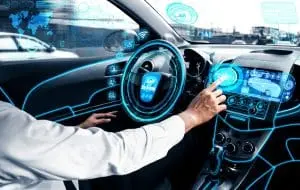 Person interacts with a futuristic holographic touchscreen interface on a car's dashboard. The interior shows digital displays and virtual controls superimposed on the steering wheel and console.