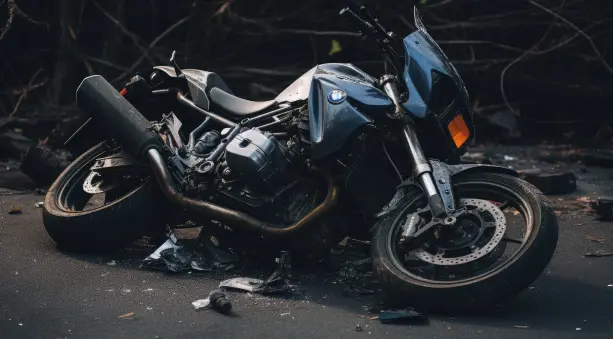 Damaged blue motorcycle lying on its side on a road, surrounded by debris with a dark background.