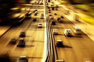 Blurred image of a busy highway with cars moving in both directions, separated by a central barrier, under a warm, golden light.