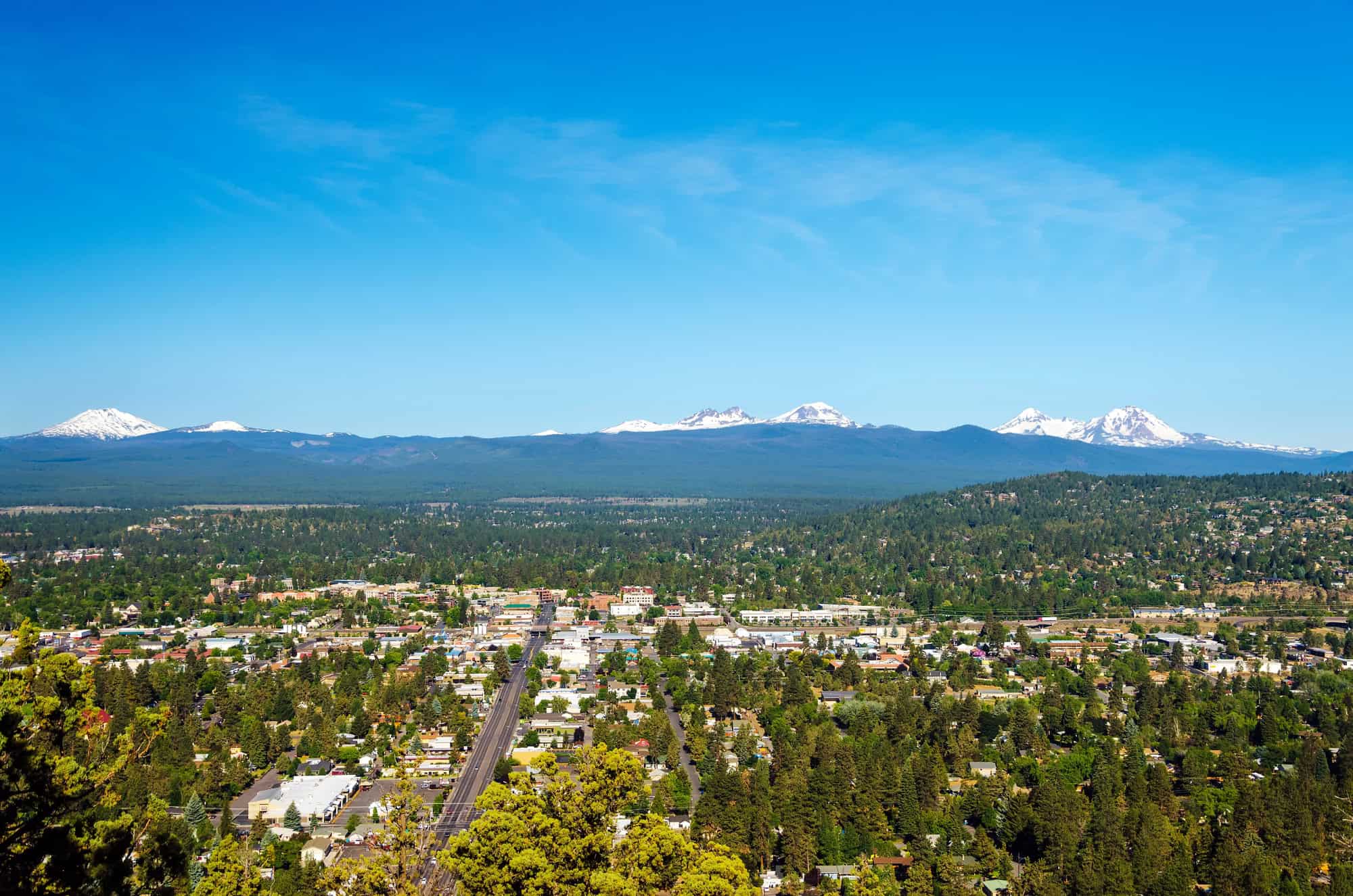 Aerial view of a city with lush greenery and distant mountains under a clear blue sky.