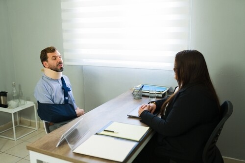 injured man wearing neck brace and arm sling meeting with attorney