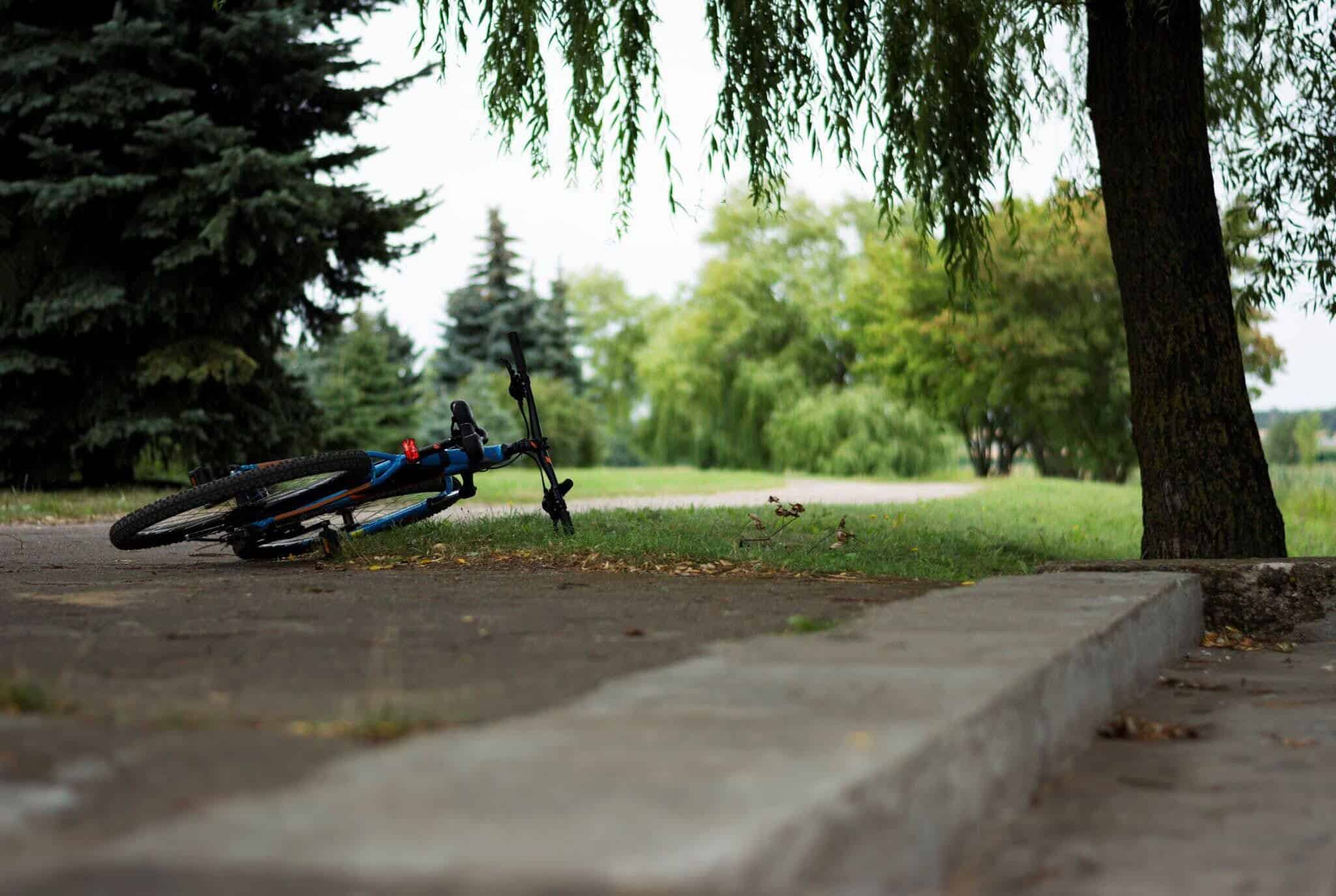 A mountain bike lying on its side on a path beside a grassy area.