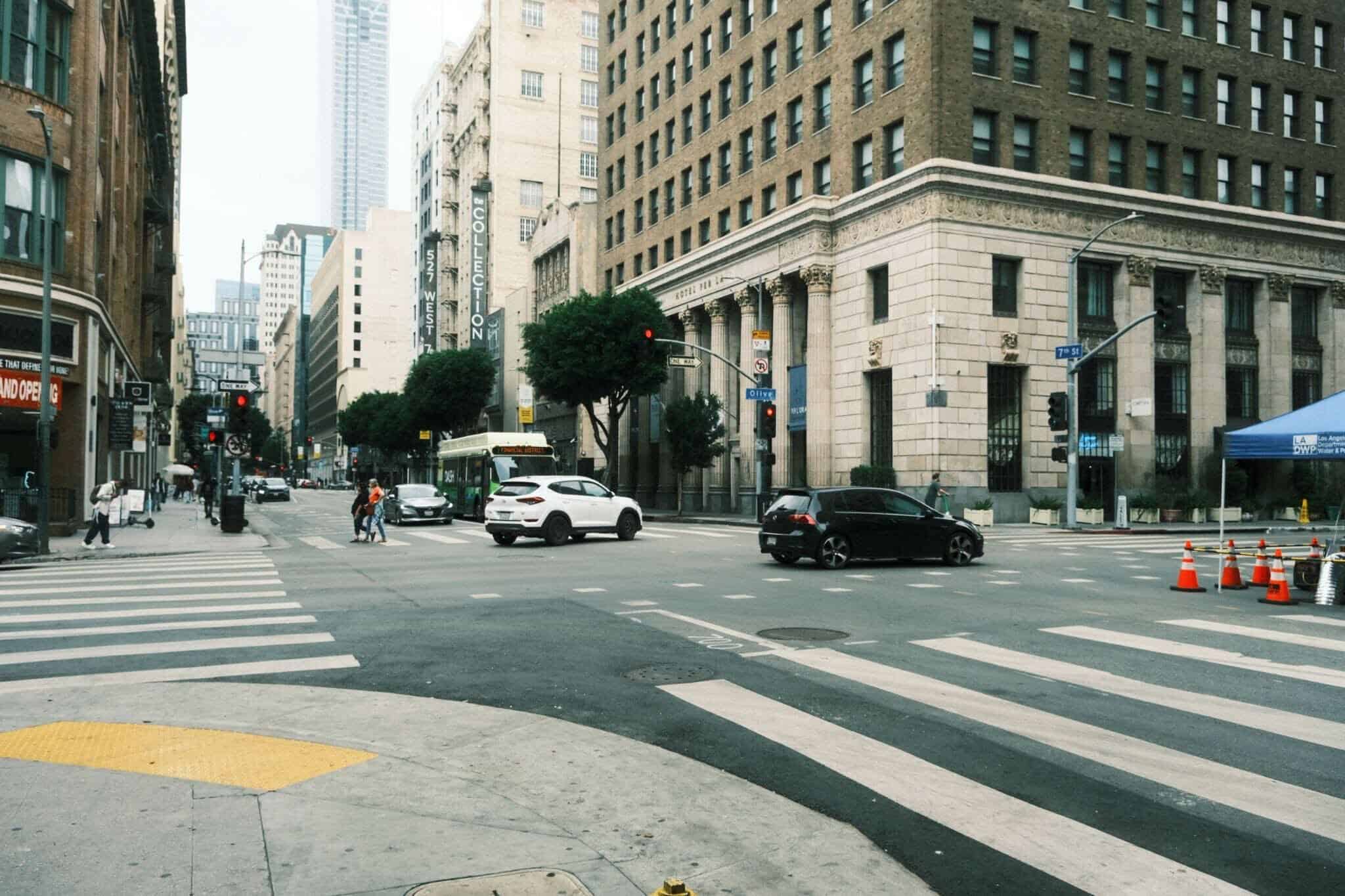 Cars and people cross through a busy downtown intersection.