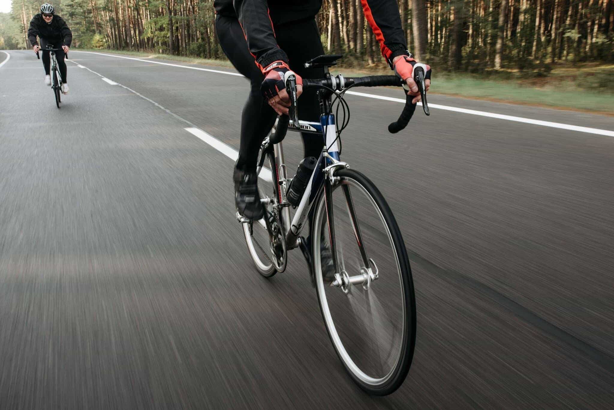 Cyclist riding on a paved road through a forest.