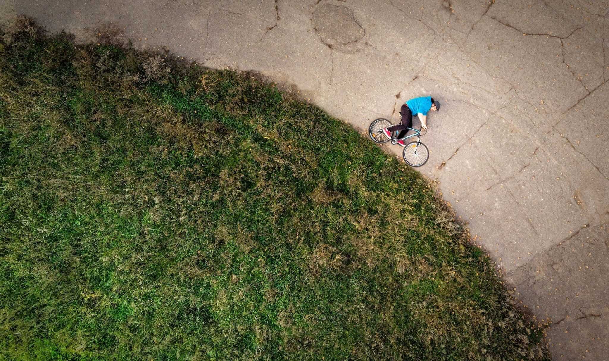 Aerial view of a cyclist riding along a cracked concrete path beside a grassy embankment.