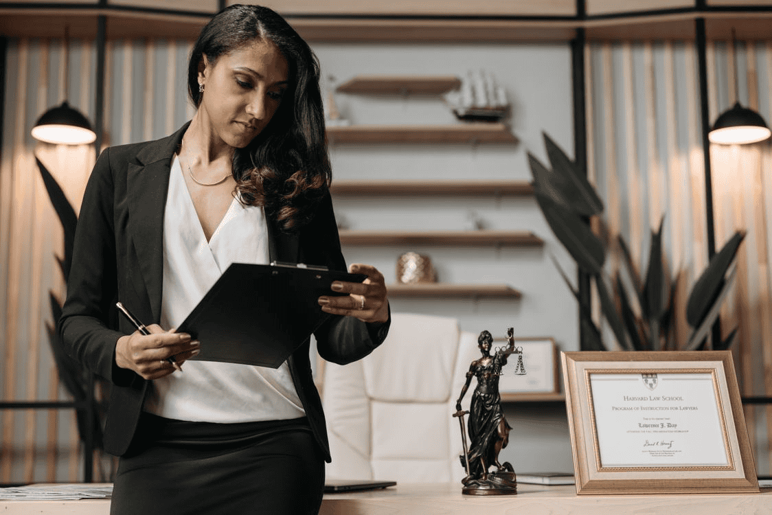 female lawyer in a black blazer standing in an office holding a clipboard
