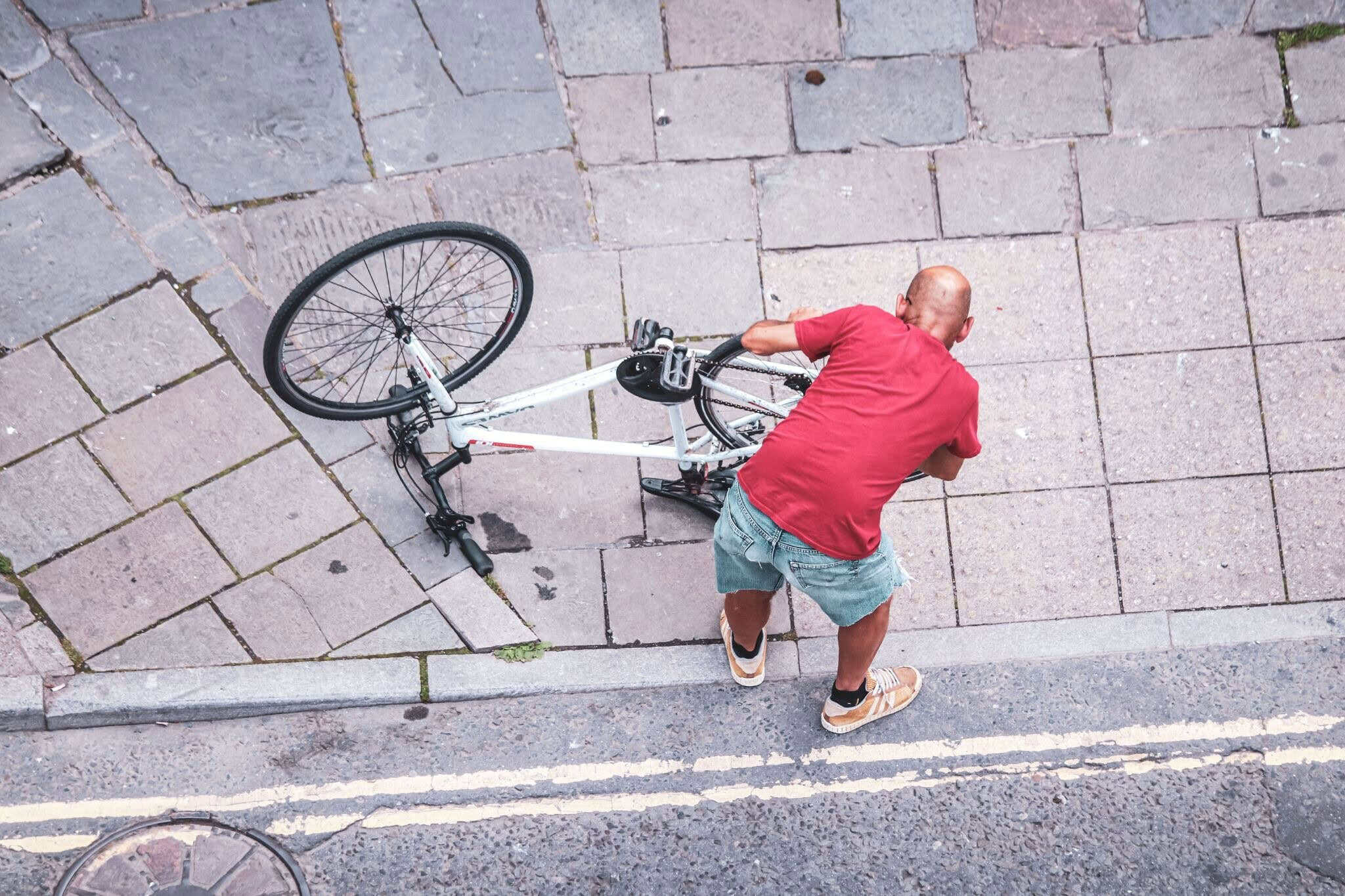 Overhead shot of a man lifting a fallen bicycle from a cobblestone pavement.