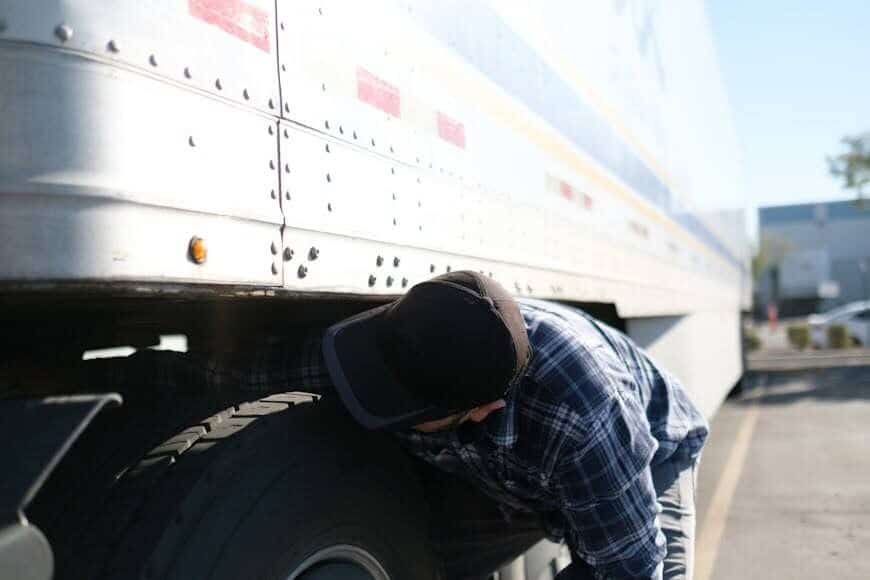 Someone wearing a black hat fixes one of the tires on a semi-truck.