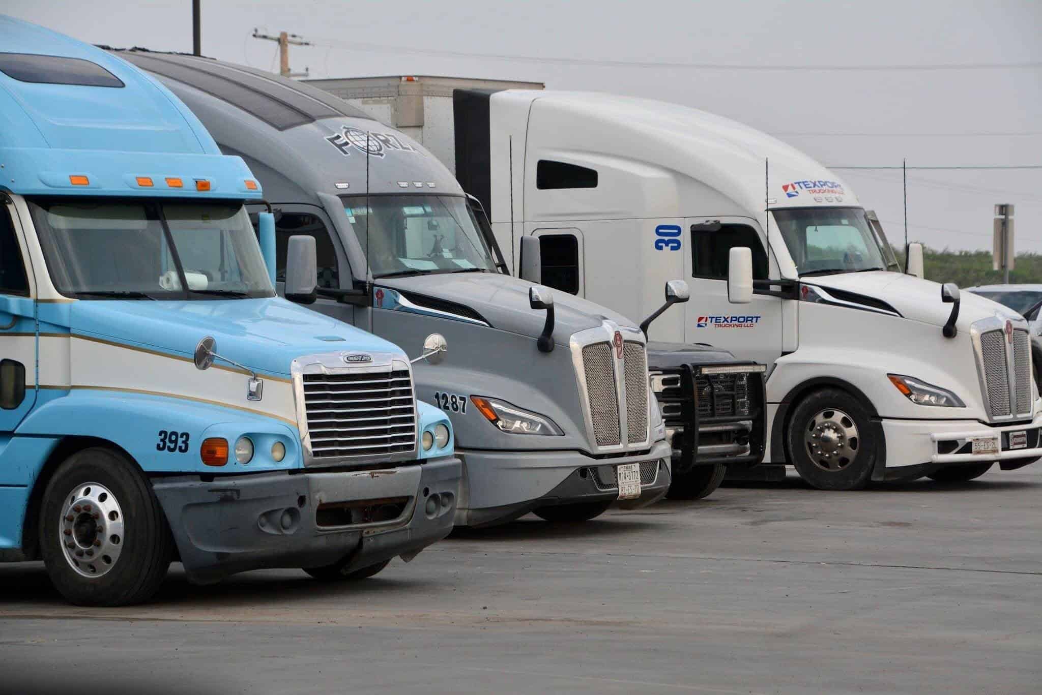 Three semi-trucks are parked next to each other in a parking lot.
