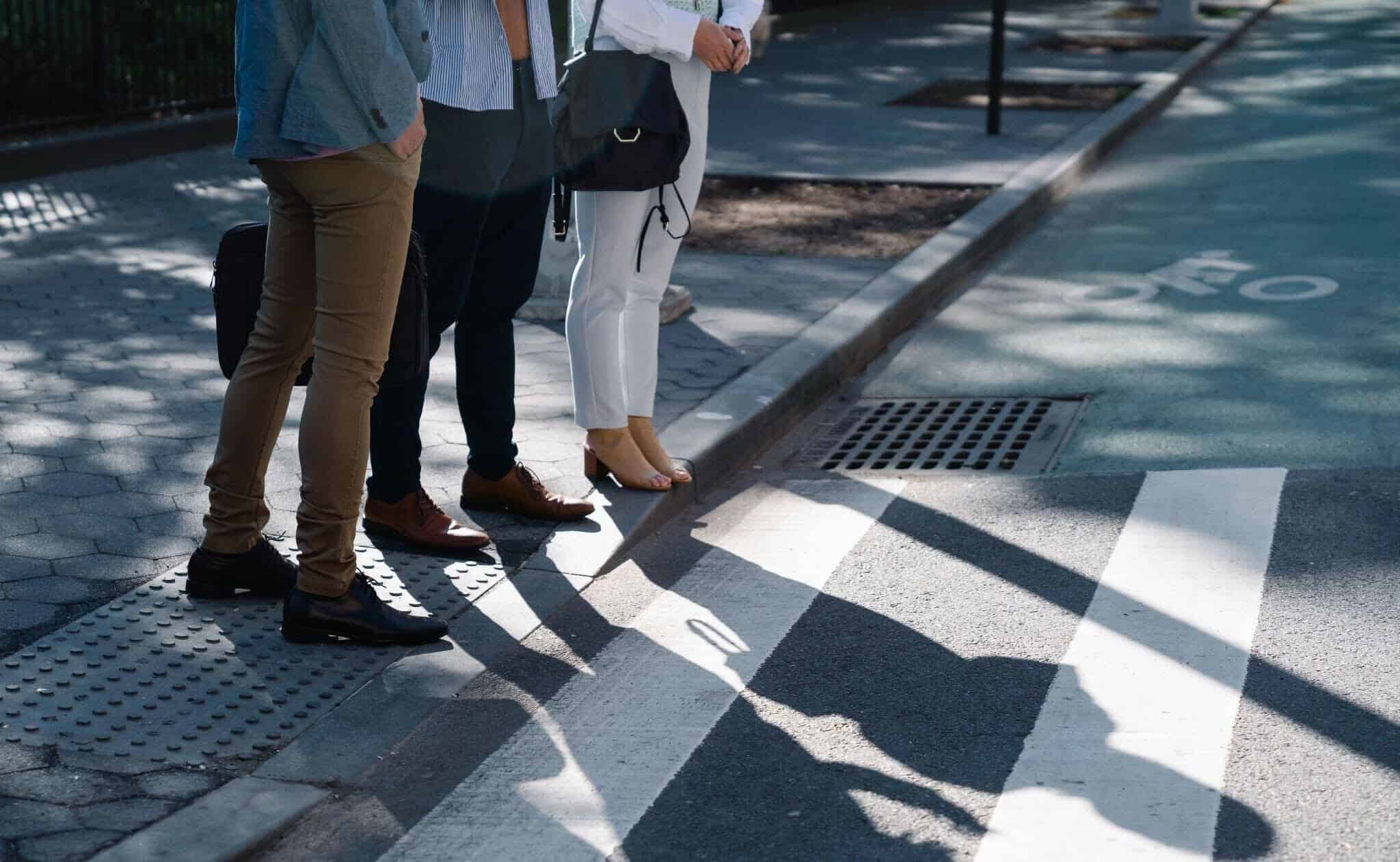Three people are waiting to cross the street using a crosswalk.