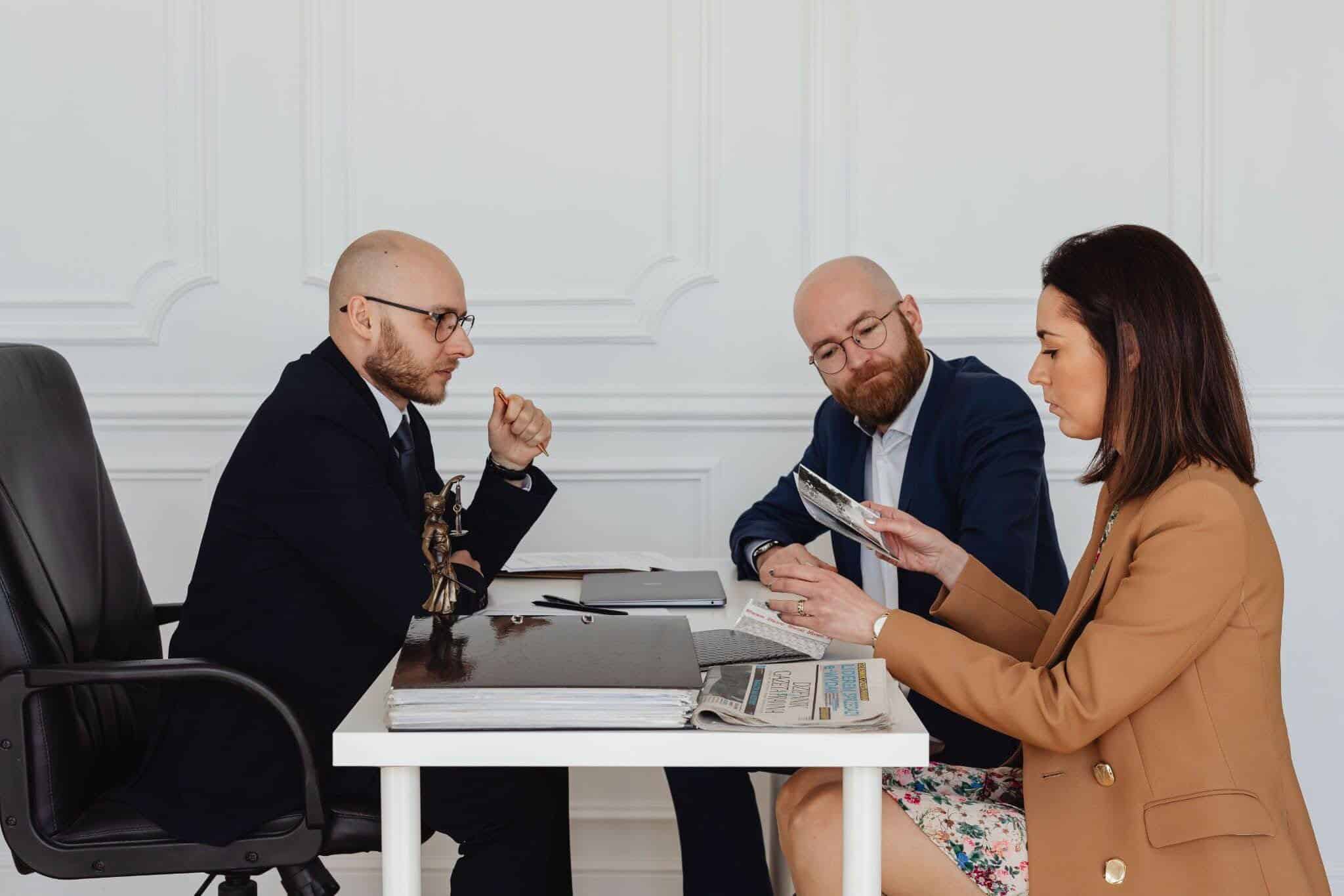A woman meeting with two lawyers is going through documents.